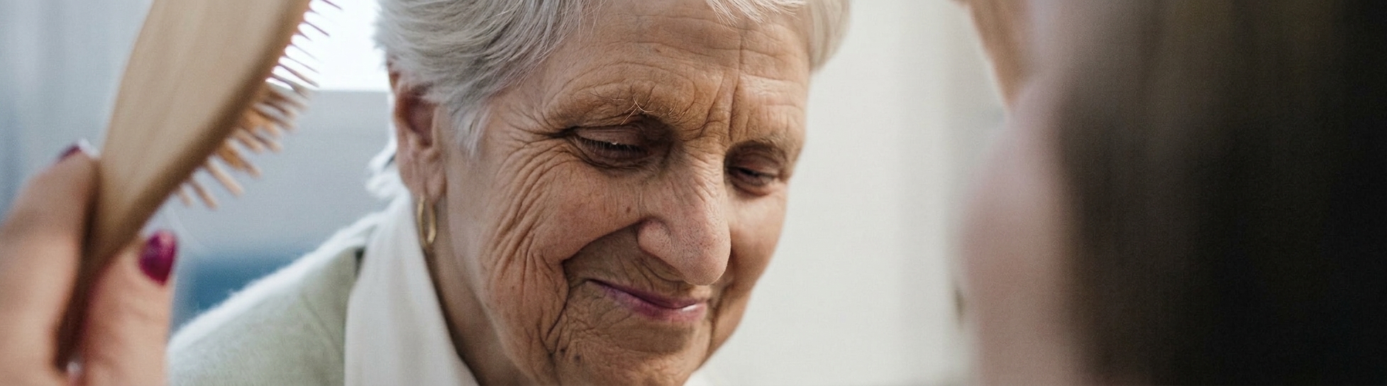 A caregiver gently brushing a smiling senior woman's hair at home